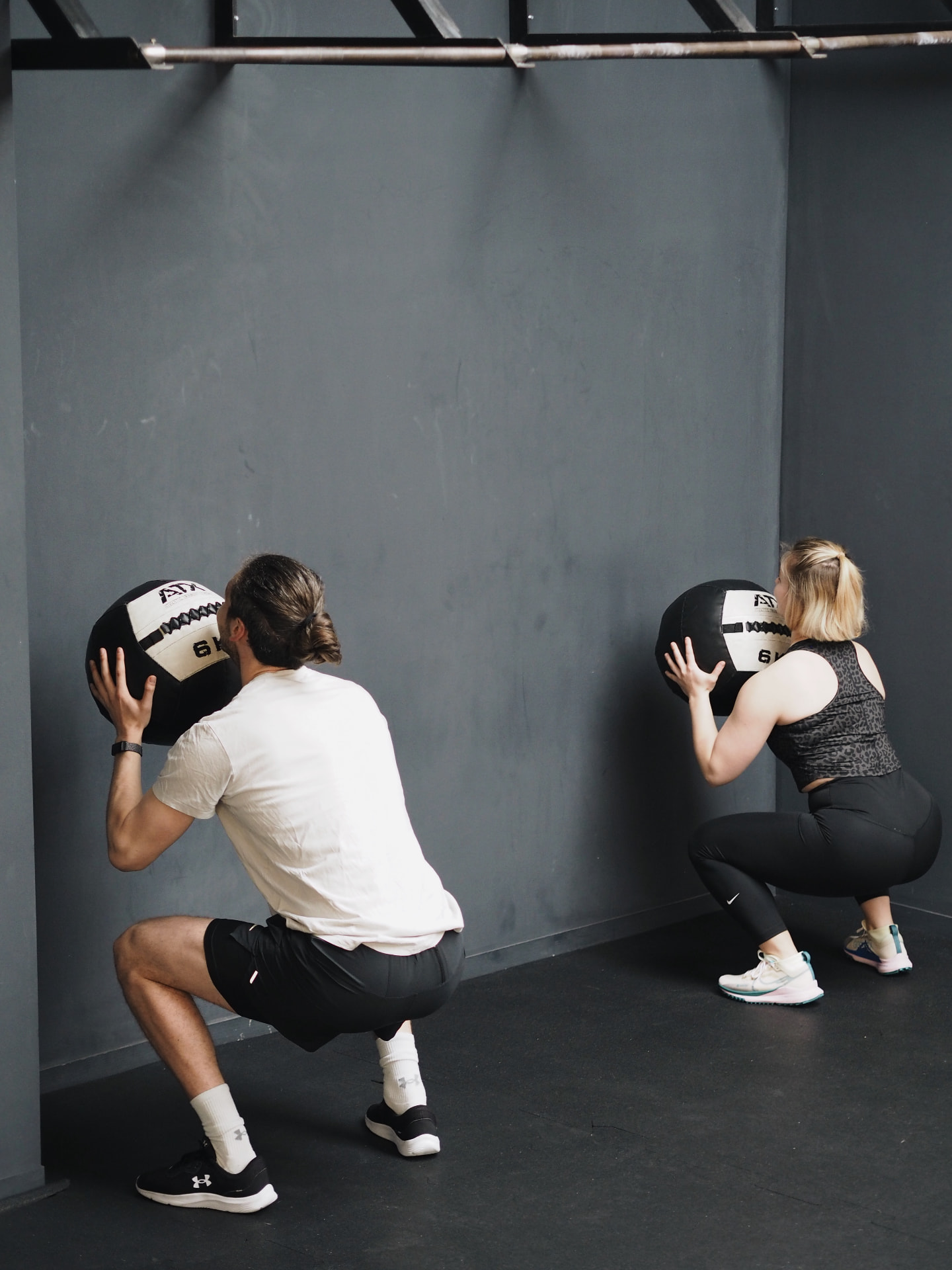 Two athletes in a wall-ball squat with medicine balls at Studio 58